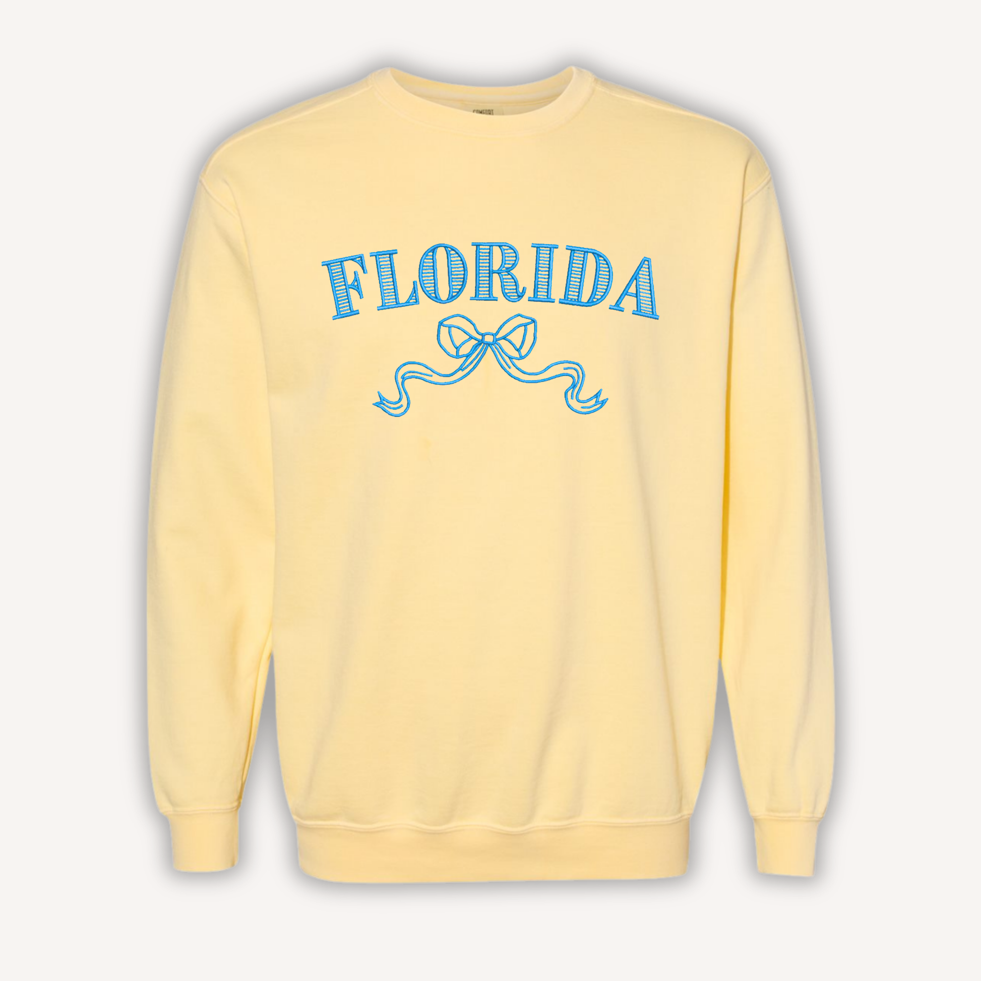 A pale yellow crewneck sweatshirt featuring the word 'FLORIDA' in blue arched letters with a ribbon graphic underneath, displayed on a clean off-white background.